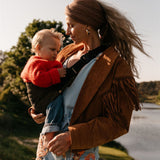 A woman carrying her toddler in the Wildride olive corduroy toddler carrier, with a river in the background.
