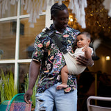 A man carrying his baby with the Wildride ergonomic carrier sling, in white linen.