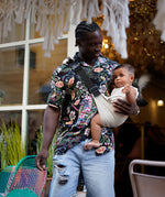 A man carrying his baby with the Wildride ergonomic carrier sling, in white linen.