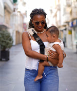 A woman carrying her baby through the city streets with the Wildride Sand Linen ergonomic baby and toddler carrier sling.