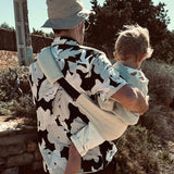 A father carrying a toddler outdoors in the sand linen Wildride toddler carrier showing the detail on the back of the strap