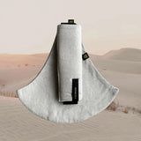Wildride toddler carrier in sand linen. A stylish hip carrier for babies with a black brand patch on the strap that's folded over the carrier's seat with a desert in the background.