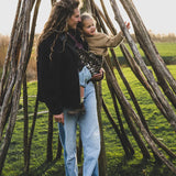 A mother carrying a toddler outdoors in the savannah Wildride toddler carrier with a child sitting on the seat and showing the  buckle detail.