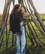A mother carrying a toddler outdoors in the savannah Wildride toddler carrier with a child sitting on the seat and showing the  buckle detail.