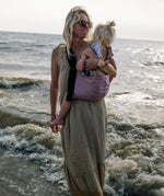 A mother carrying a toddler on the beach in the vintage rose Wildride toddler carrier with a child sitting on the seat and showing the front detail on the strap and seat