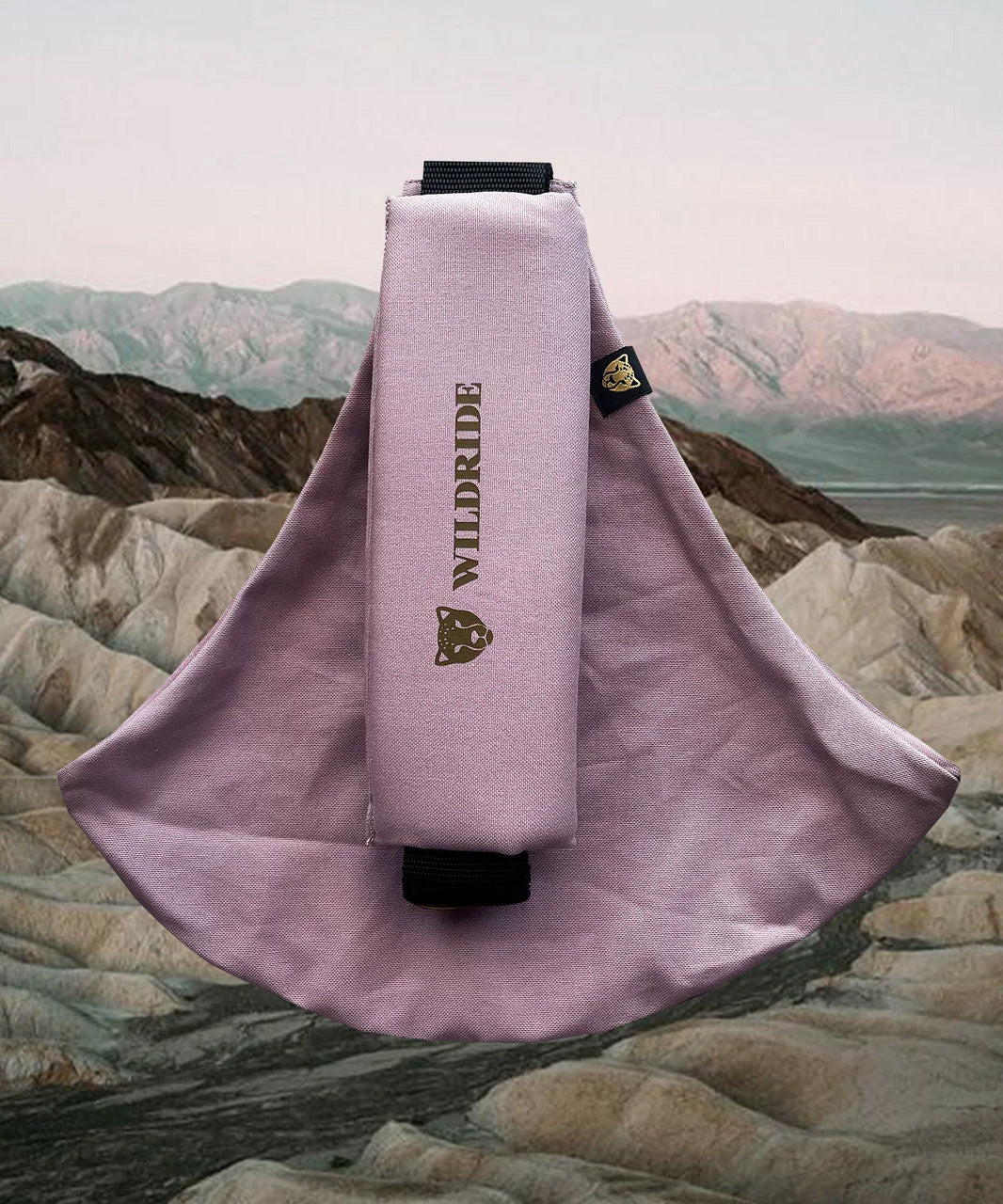 Wildride toddler carrier in vintage rose. A 100% cotton seat stylish hip carrier for babies with brand name in brown on the strap that's folded over the carrier's seat with a mountain scape in the background.