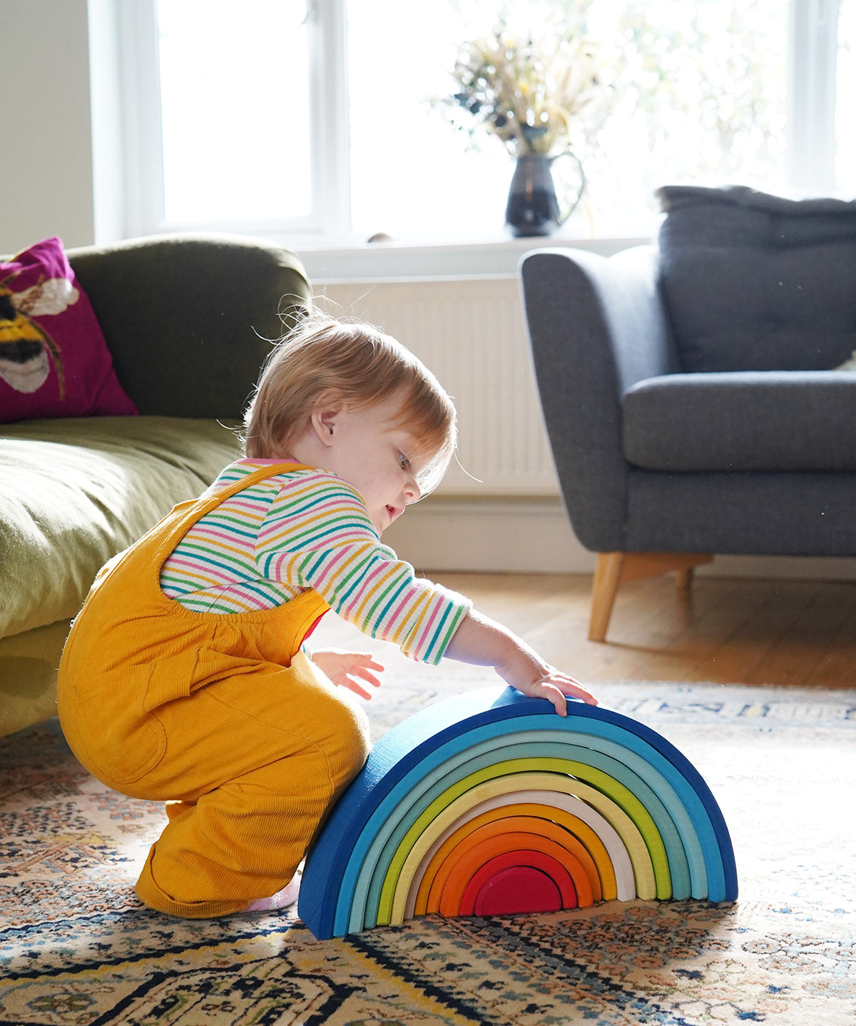 A child crouching down besides the Grimm's Gwawr Sunrise 12 Piece Rainbow.
