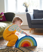 A child crouching down besides the Grimm's Gwawr Sunrise 12 Piece Rainbow.