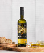 A 250ml bottle of Zaytoun Organic Extra Virgin Olive Oil on a wooden board next to bread and glass dishes containing some olive oil.