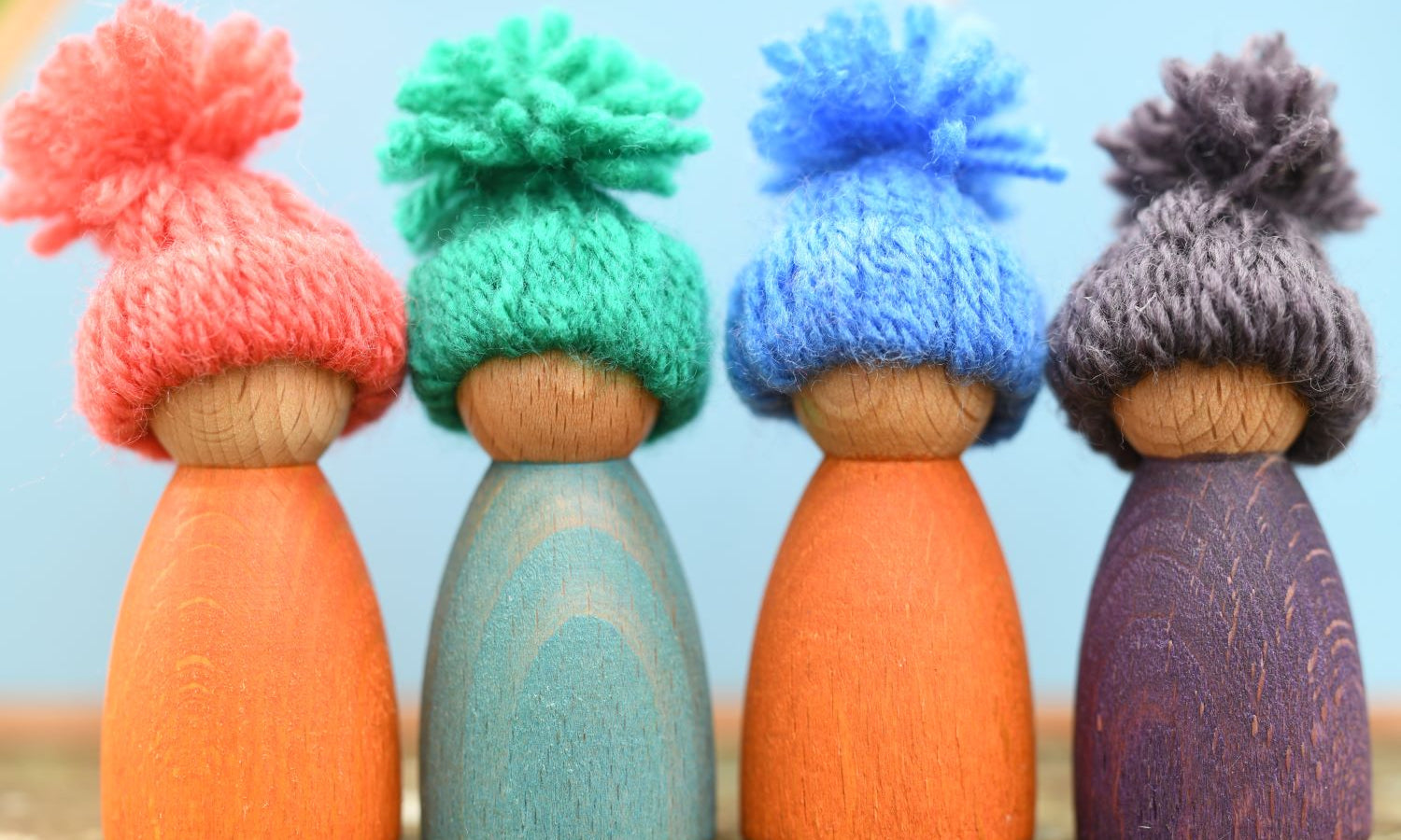 A group of 4 peg dolls each wearing a handmade woolly hat