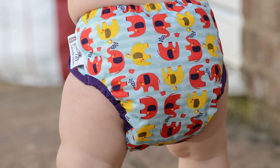 A baby wearing a reusable nappy with a playful elephant print in yellow and red
