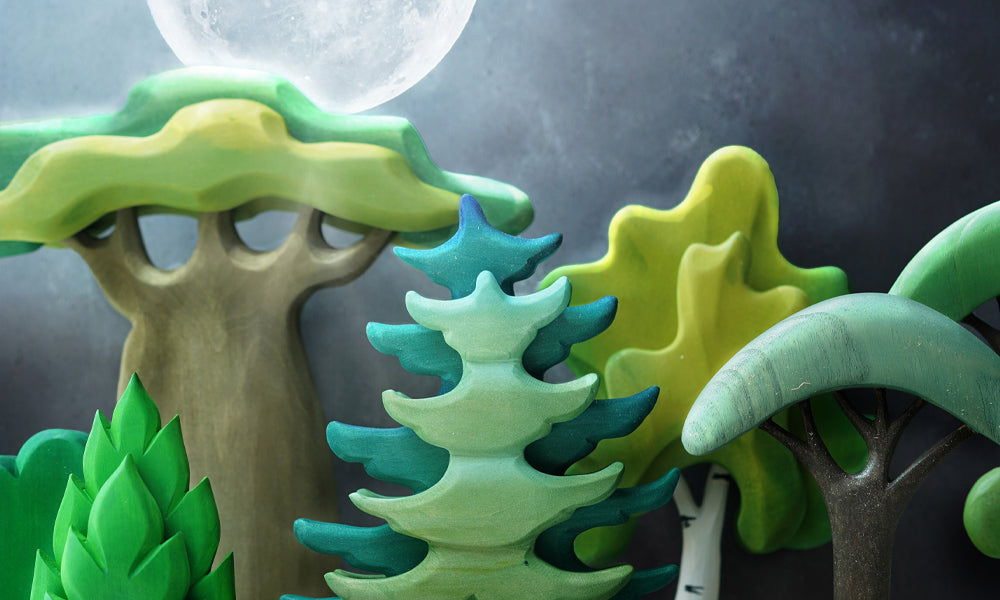 A line of Bumbu wooden trees against a dark background with a full moon in the distance to represent 'The Moon Before Yule' blog by Babipur.