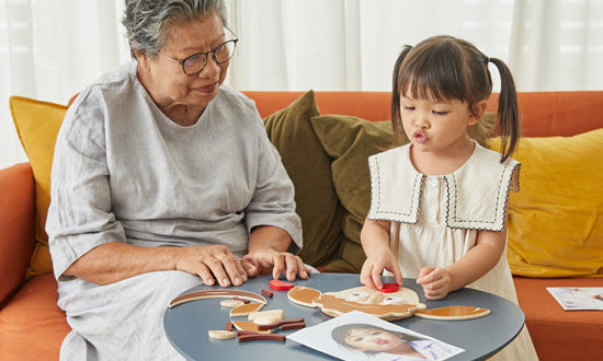 Image of elderly woman and young girl playing with a 'Build a Face' wooden toy