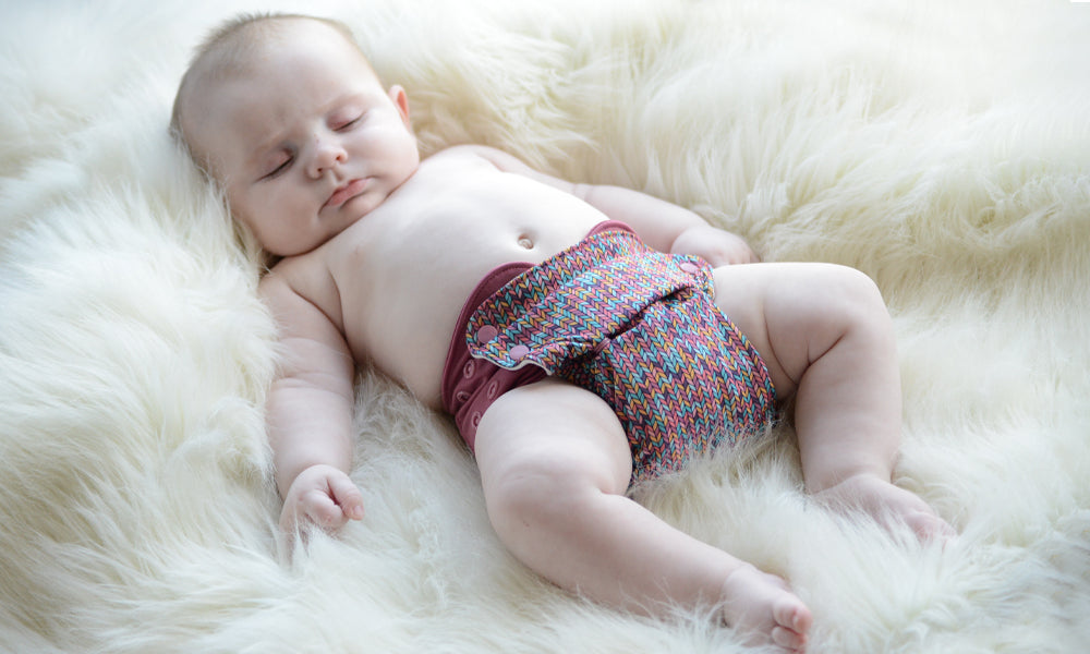 Baby asleep on a fluffy blanket wearing a Grovia reusable cloth night nappy to represent 'A Complete Guide To Using Reusable Night Nappies' blog by Babipur.