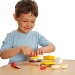 Child building a sandwich with the Erzi Cutting Sandwich Wooden Play Food Set at a table.