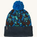 A blue Patagonia bobble beanie with different shapes and patterns on a cream background.