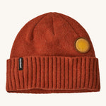 A red beanie with the Patagonia logo and sun badge on the front on a cream background.