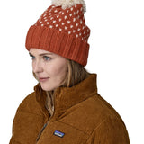 A female adult wearing the red Patagonia  beanie with a cream pompom 