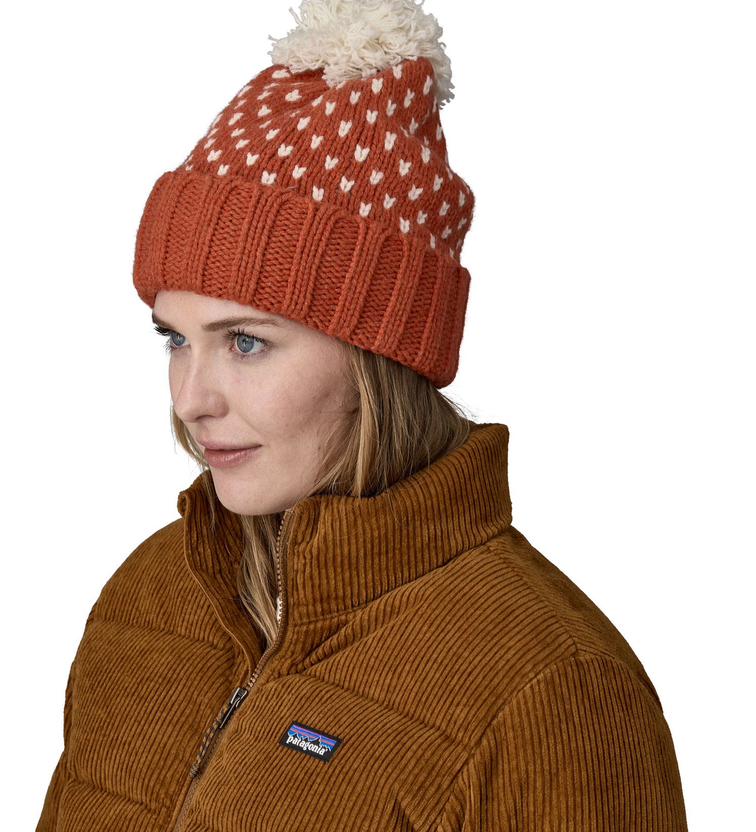 A female adult wearing the red Patagonia  beanie with a cream pompom 
