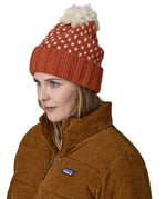 A female adult wearing the red Patagonia  beanie with a cream pompom 