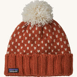 A red Patagonia beanie with a cream pom pom and cream patterns on a cream background.