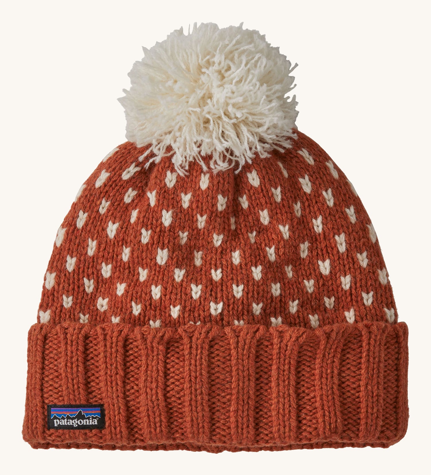 A red Patagonia beanie with a cream pom pom and cream patterns on a cream background.