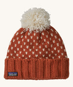 A red Patagonia beanie with a cream pom pom and cream patterns on a cream background.