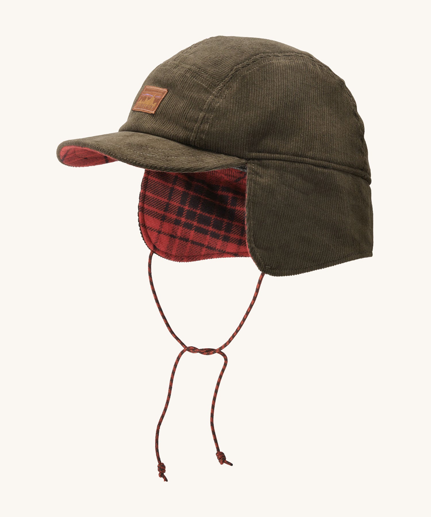 A brown cord Patagonia earflap cap with a red check design on the inside with the flaps down on a cream background.