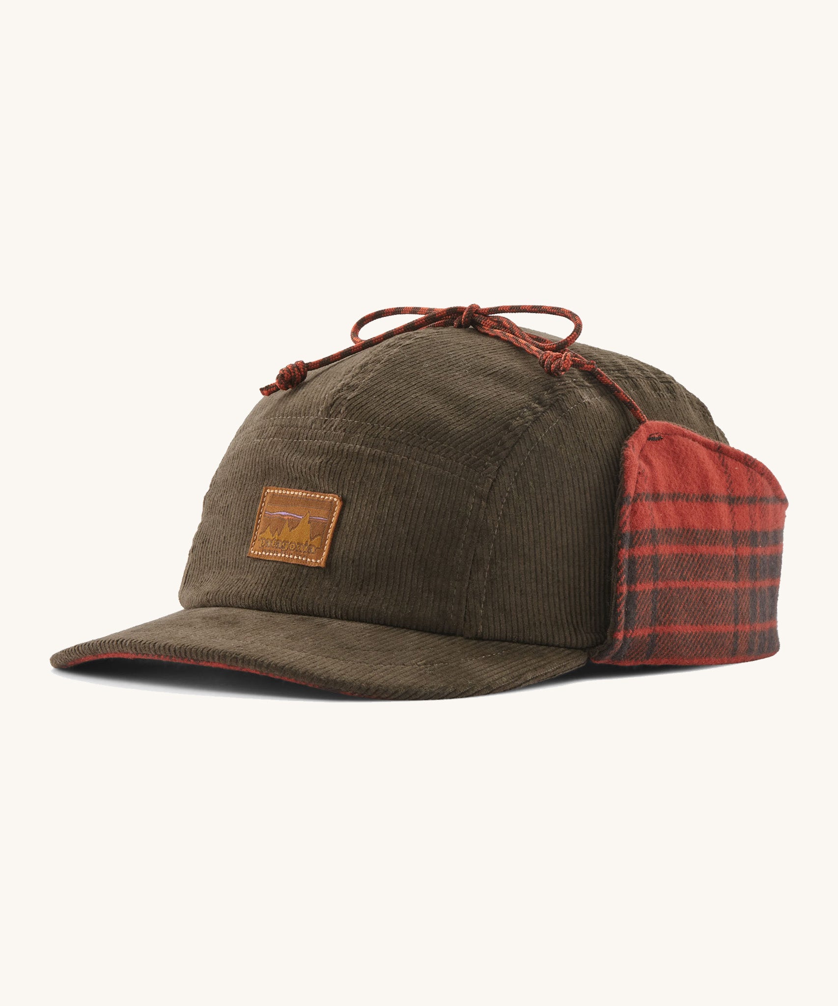 A brown cord Patagonia earflap cap with a red check design on the inside on a cream background.
