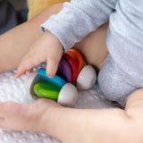 Plan Toys Rainbow Car Rattle Toy is a solid rubber wood sensory toy for babies painted in bright rainbow colours. Close up of baby playing.