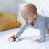 Plan Toys Rainbow Car Rattle Toy is a solid rubber wood sensory toy for babies painted in bright rainbow colours. Baby pushing it along.