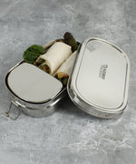 A close up of the A slice of green oval lunchbox with mini container showing various food items inside the main compartment