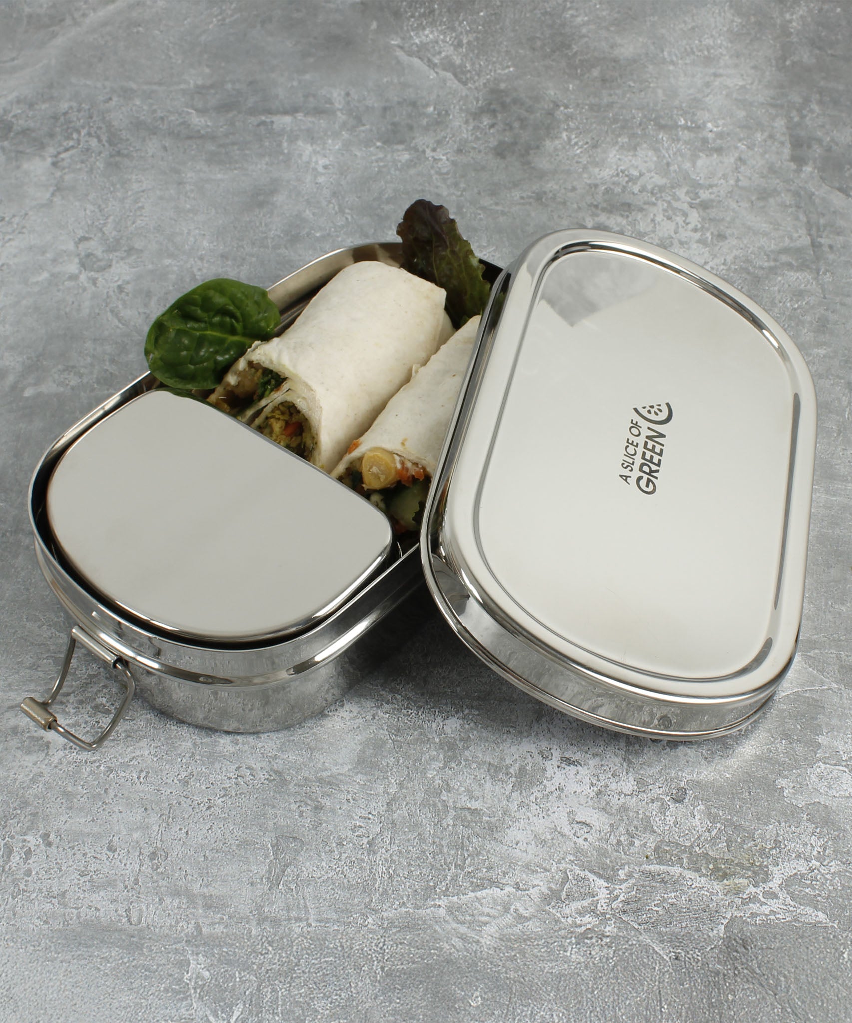 A close up of the A slice of green oval lunchbox with mini container showing various food items inside the main compartment