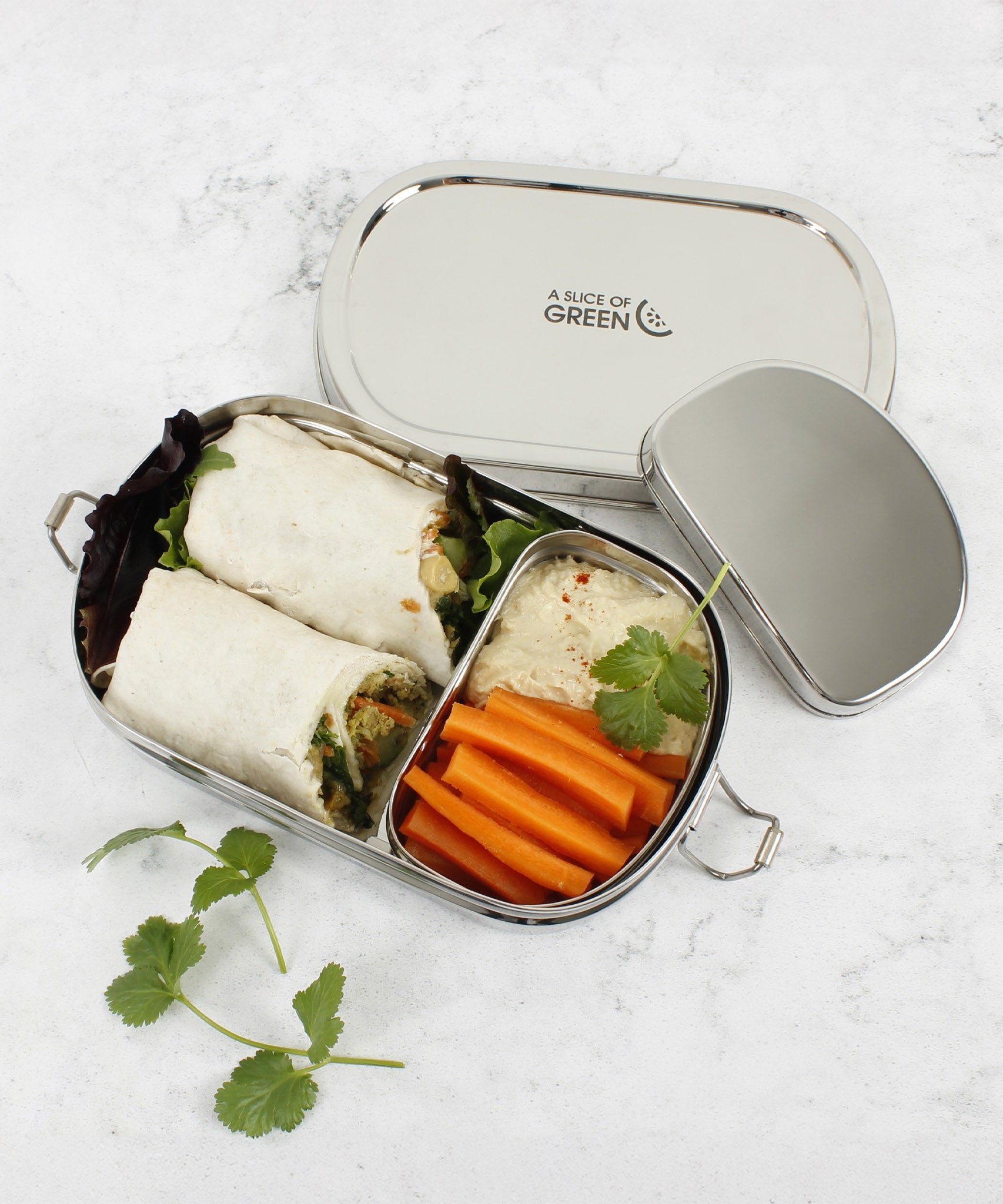 A top down image of the A slice of green oval lunchbox with mini container on a stone surface with different food items inside