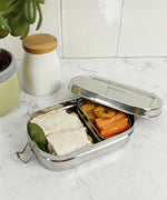 A slice of green oval lunchbox with mini container on a marble kitchen worktop