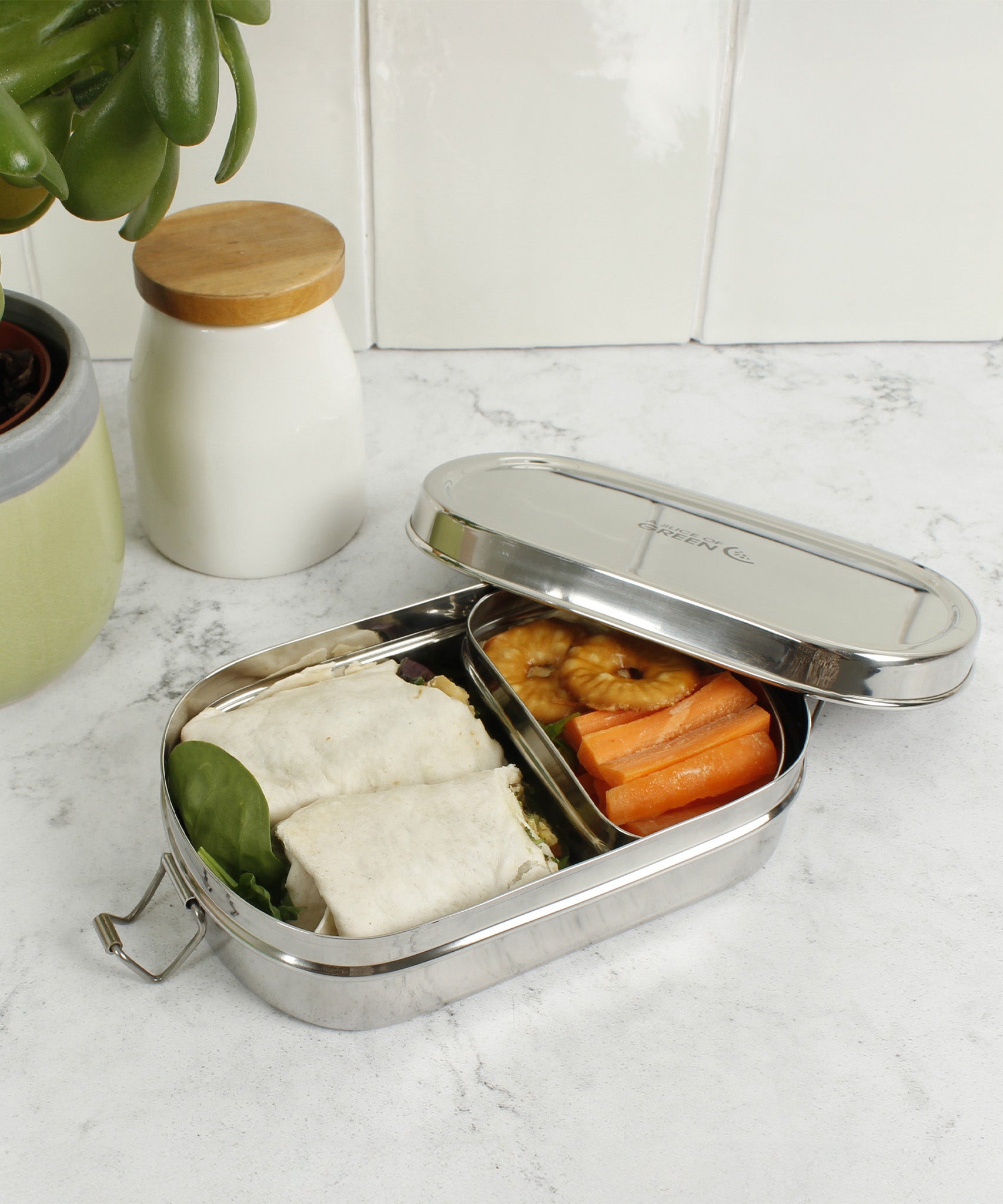 A slice of green oval lunchbox with mini container on a marble kitchen worktop