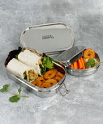 A slice of green oval lunchbox with mini container on a stone surface showing various food items in each container