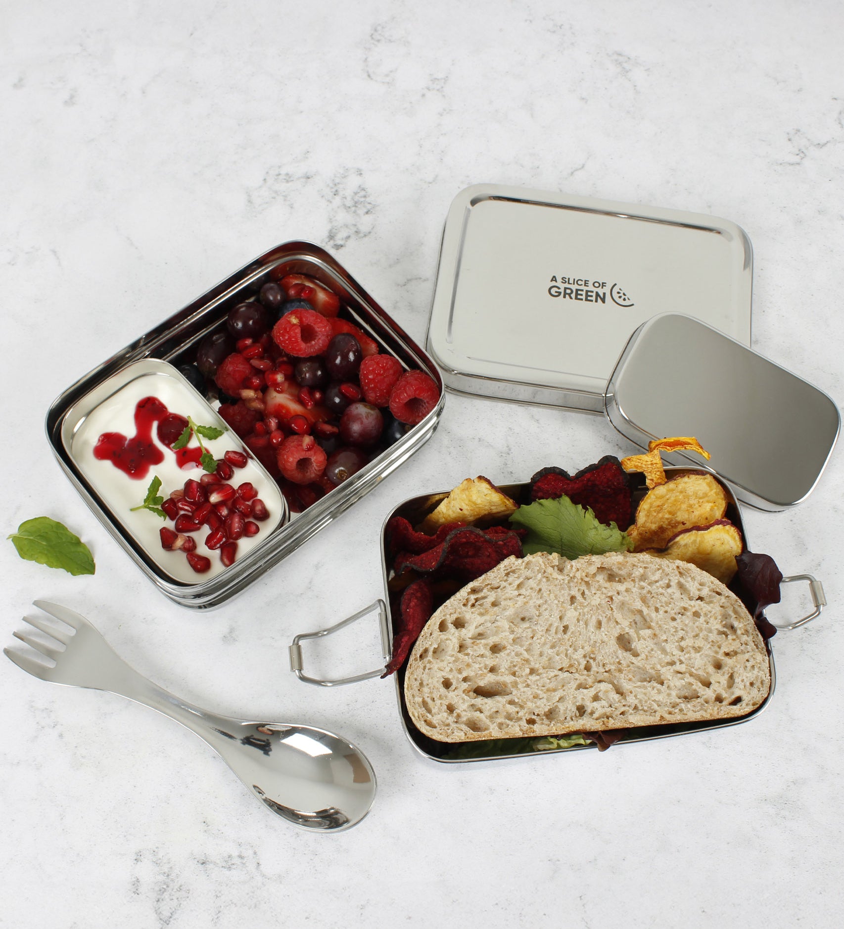 A top down image of A slice of green two tier lunchbox with mini container showing various food and fruit items inside each compartment