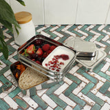 A slice of green two tier lunchbox with mini container resting on a kitchen counter 