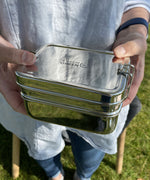 A close up of an adult holding the A slice of green two tier lunchbox with mini container 