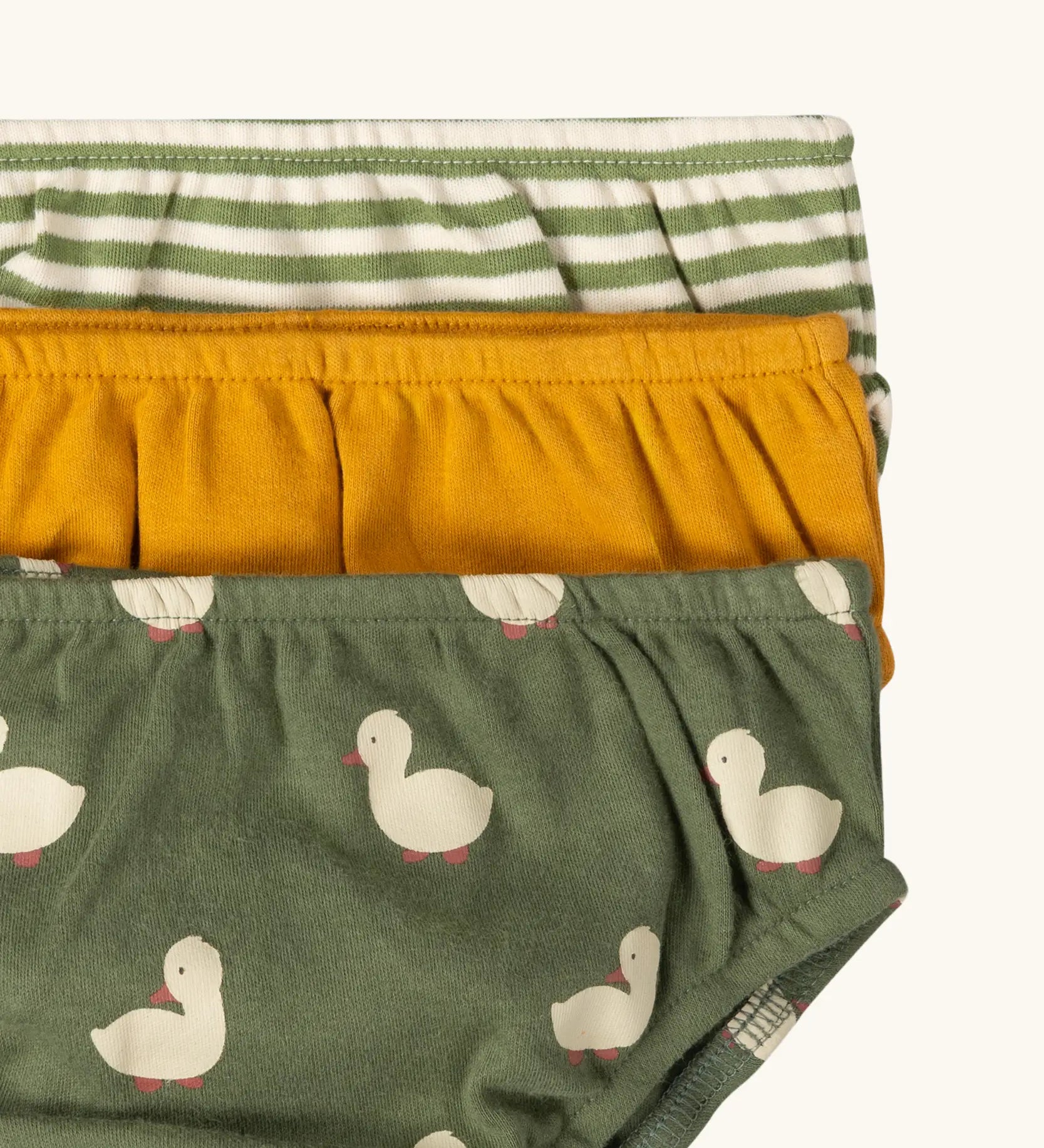 Close up of the elasticated waistband on the Little Green Radicals organic cotton underwear in a 3 pack. Brief style pants one with a ducks print on a green background, one yellow gold, one green and white stripes. 