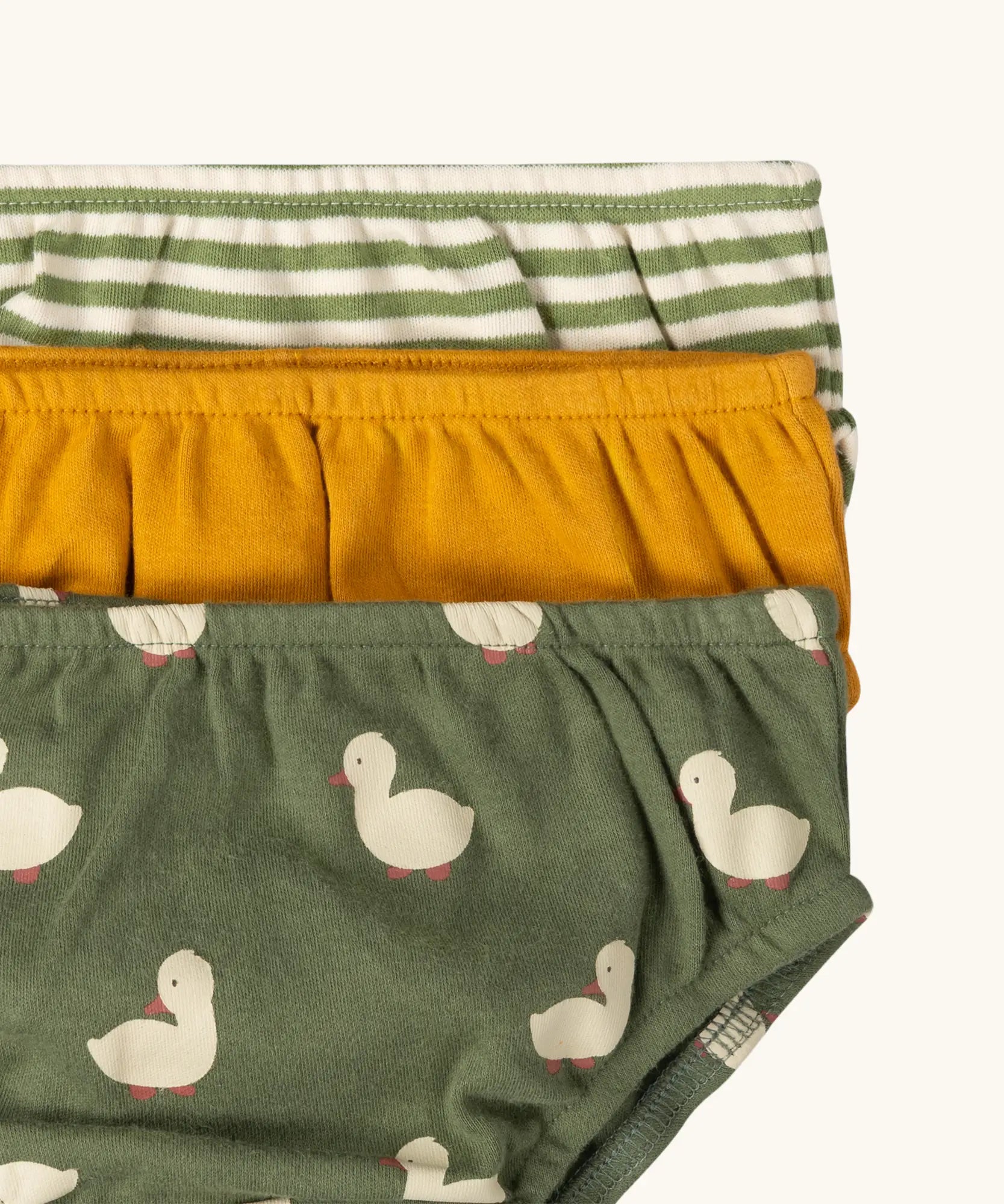 Close up of the elasticated waistband on the Little Green Radicals organic cotton underwear in a 3 pack. Brief style pants one with a ducks print on a green background, one yellow gold, one green and white stripes. 