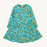 The Frugi Sofia skater dress with a wild woods print design on a green background. The print features flowers and toadstools.