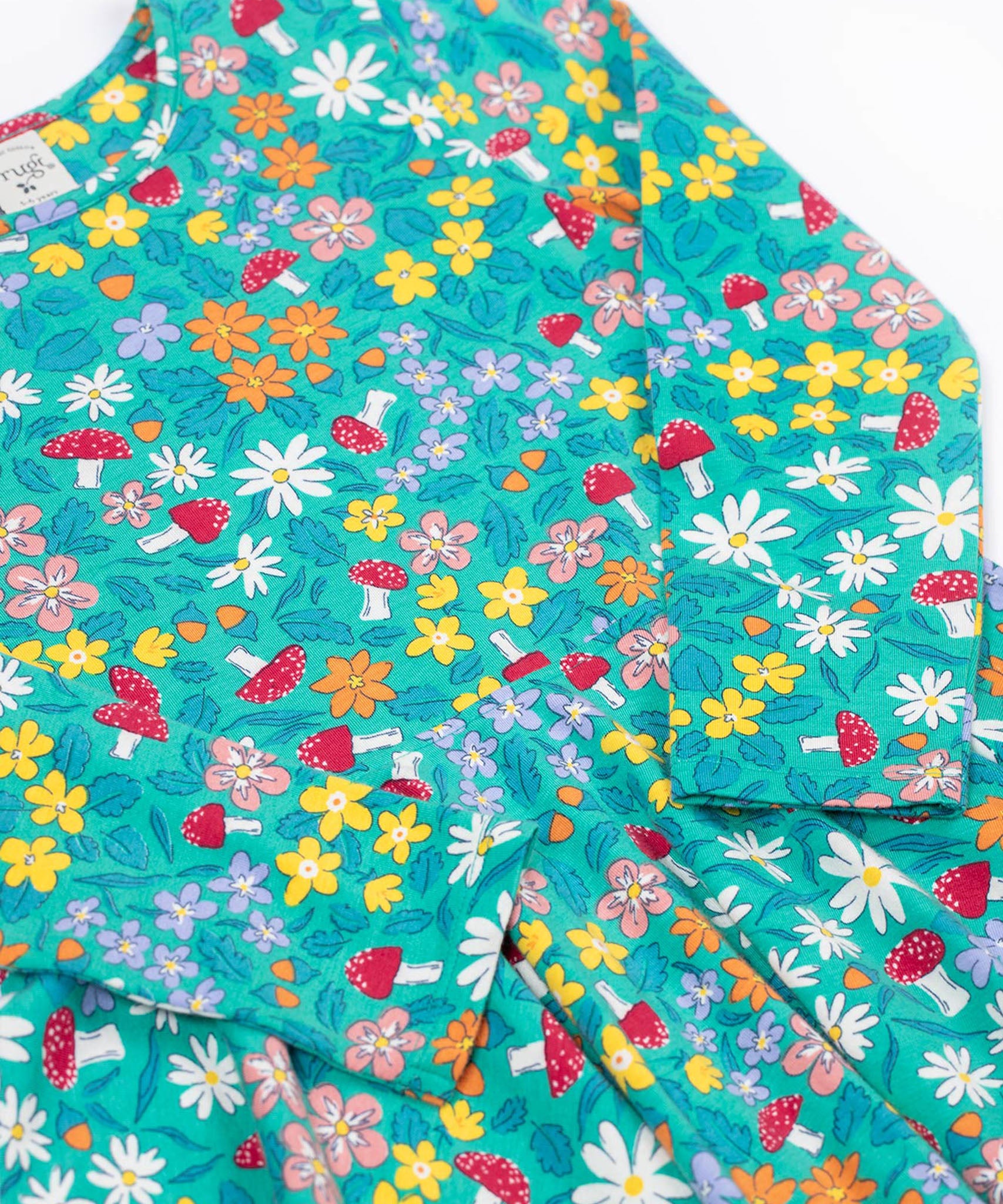 A close up of the Frugi Sofia skater dress with a wild woods print design on a green background. The print features flowers and toadstools.