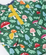 A close up view on the Frugi fun-guys snuggle fleece. A mushroom themed print on a green coloured background. 