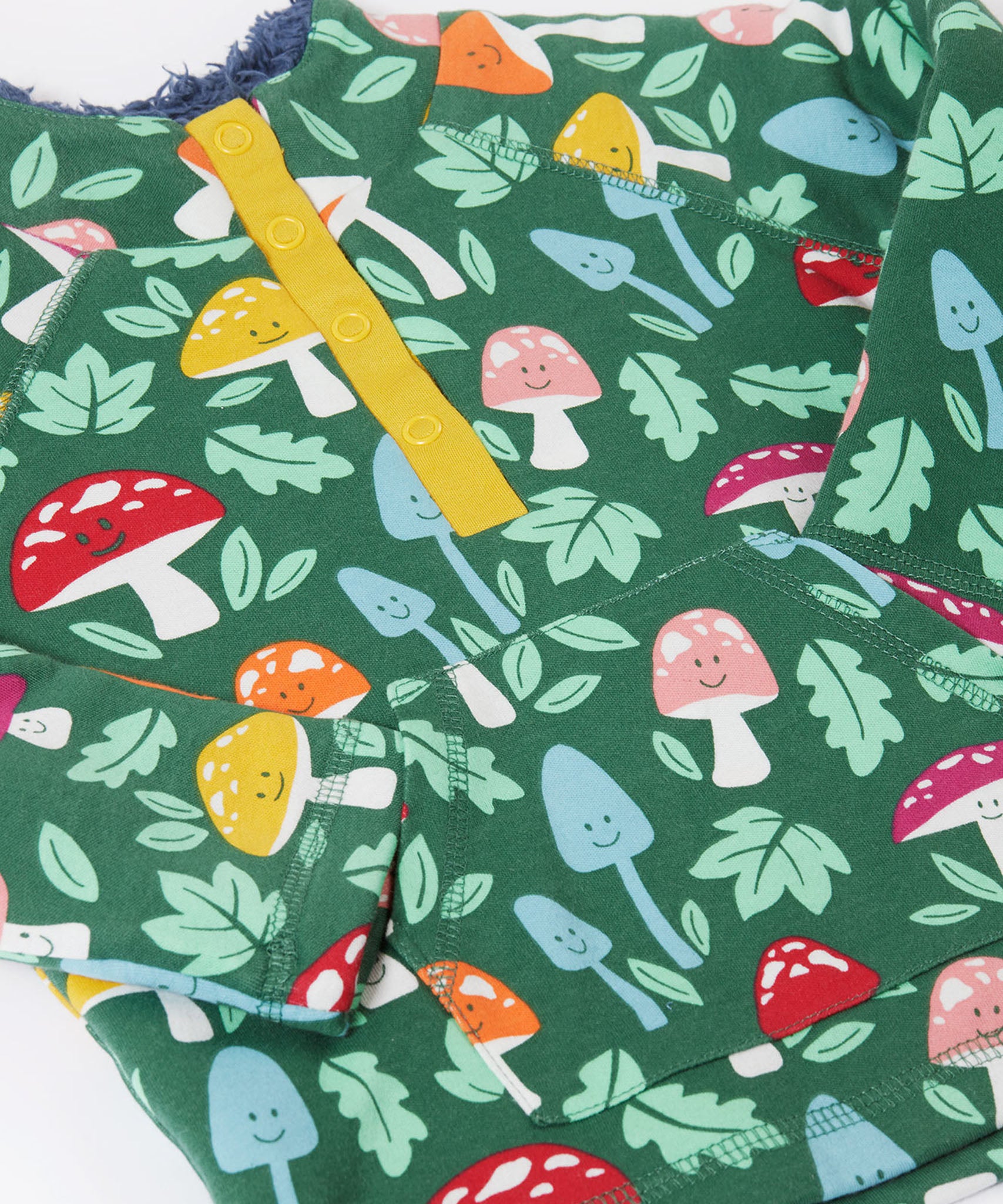 A close up view on the Frugi fun-guys snuggle fleece. A mushroom themed print on a green coloured background. 