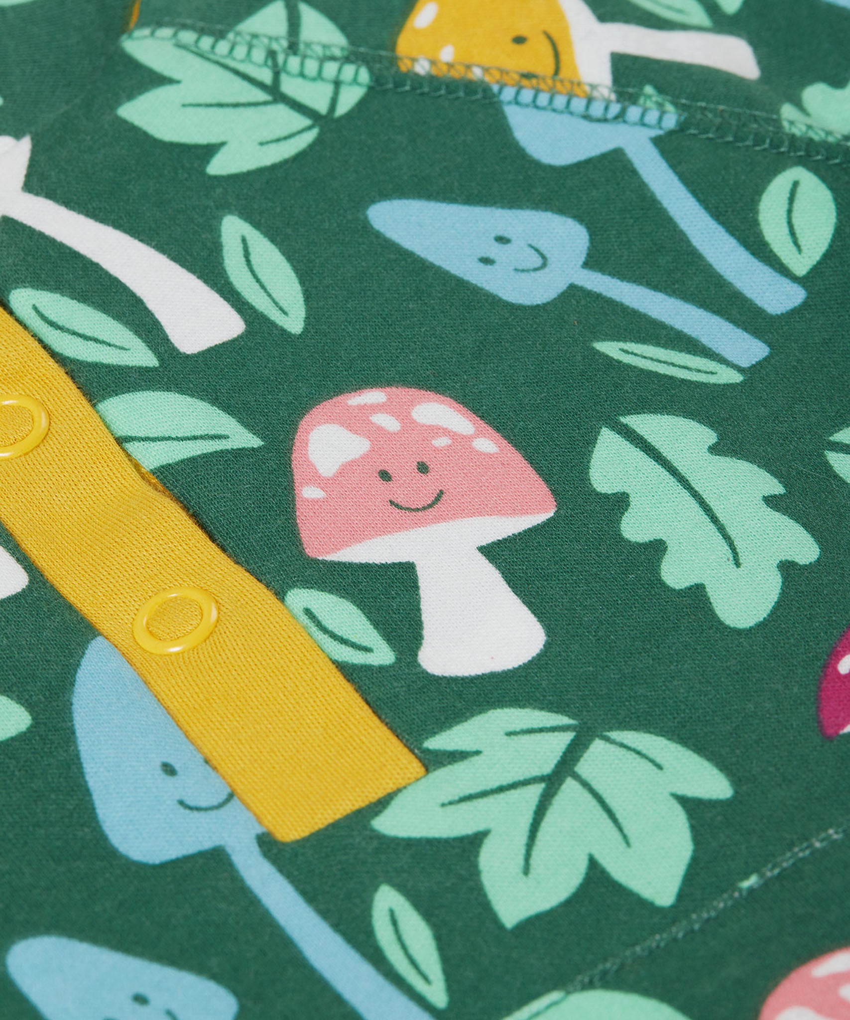 A super zoomed in close up of the Frugi fun-guys snuggle fleece. A multi-coloured mushroom themed print on a green coloured background. 