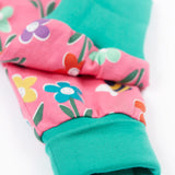 A close up of the turquise cloured turn up leg cuffs on the Frugi fun flowers print parsnip pants. The fun flowers print features multi-coloured flowers and bees on a pink background with turquoise coloured waistband and leg cuffs.