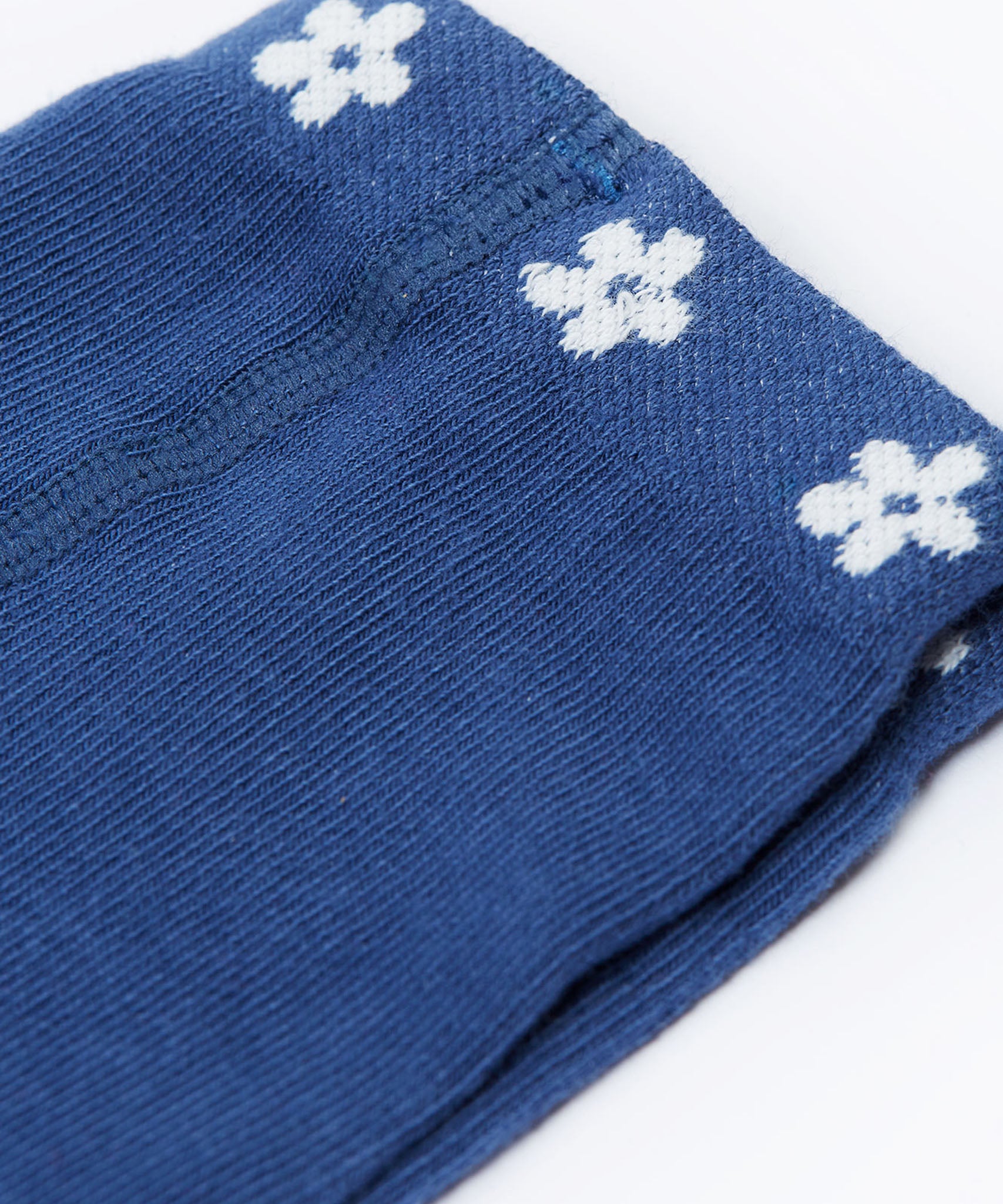 A close up of the waist band on the Frugi Norah navy blue Flowers design footed tights. A navy waist band with little white flowers all around. 