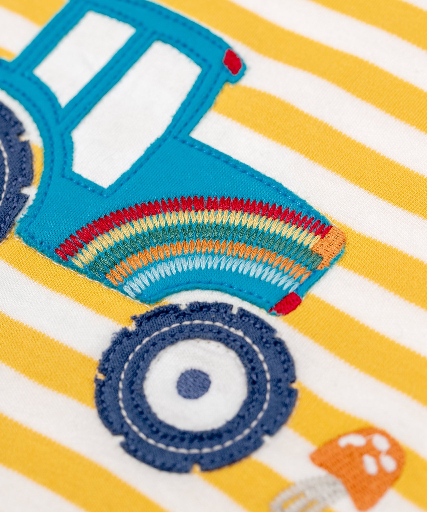 A super close up view of the embroidered rainbow detail on the tractor applique on the Frugi Orion Bumblebee tractor design long sleeved kids top.